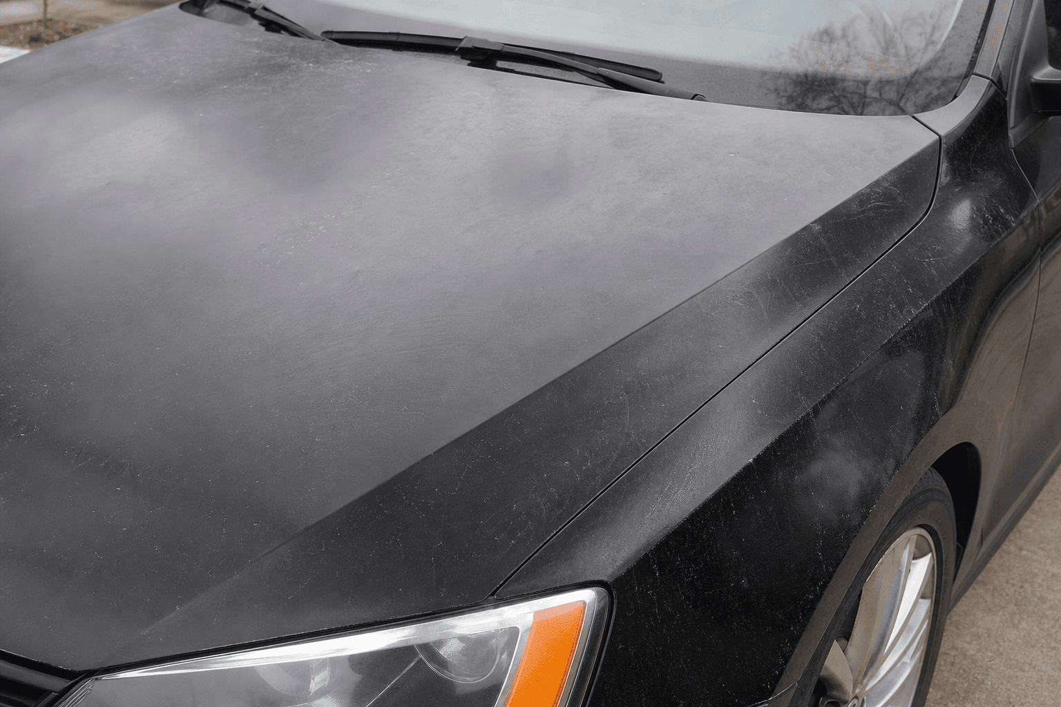 Before exterior detailing — dull paint with swirl marks on black sedan
